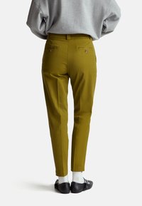 Pantaloni verde oliva con una vestibilità sartoriale e gambe affusolate. Presentano due tasche posteriori con bottoni e un tessuto liscio e testurizzato.