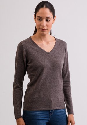 Brązowy sweter z długim rękawem w serek, wykonany z teksturowanej tkaniny, o dopasowanym kroju i ściągaczach przy mankietach, zestawiony z niebieskimi dżinsami.