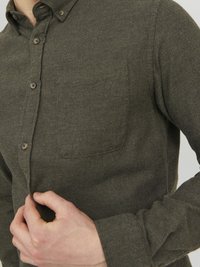Camisa de botones verde oscuro hecha de tejido texturizado, con un bolsillo en el pecho y puños abotonados. La camisa tiene un diseño de cuello clásico.