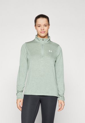 Haut de sport vert clair à manches longues et fermeture éclair quart de manière texturée, avec un petit logo sur la poitrine. Associe avec des leggings foncés.