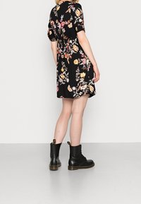 Robe noire à fleurs avec des manches courtes à volants, taille élastique et coupe au genou. Associée à des bottes noires à lacets avec une semelle épaisse.