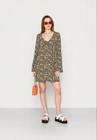 Vestido preto floral com mangas longas, decote em V e um corte solto. Combinado com sandálias brancas e uma bolsa laranja com alça de corrente.