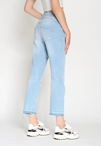 Ljusblå jeans med rak klippning, fransad fåll och två bakfickor. Parat med vita och svarta träningsskor.