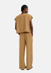 Brązowy lniany crop top i szerokie spodnie. Top ma luźny krój z krótkimi rękawami, a spodnie charakteryzują się gładką fakturą i bocznymi kieszeniami.