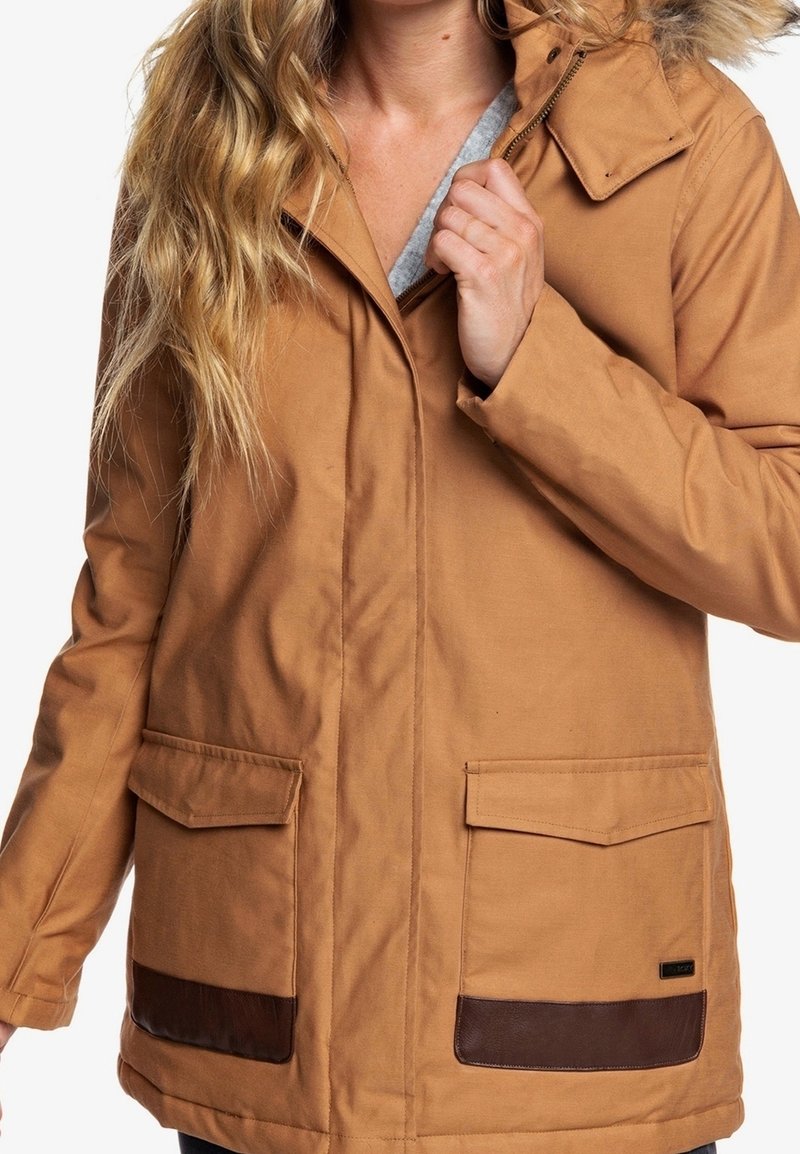 Chaqueta marrón con capucha, cierre frontal, dos grandes bolsillos y detalles en cuero marrón. La tela parece duradera con una textura suave.