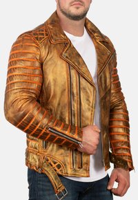 Giacca da motociclista in pelle marrone invecchiata con dettagli arancioni, dettagli a costine sulle maniche, doppie cerniere e vita con cintura.