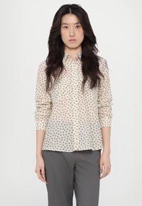 Sheer, cream blouse with small brown floral patterns, button-down front, long sleeves, and a pointed collar. Paired with gray trousers.