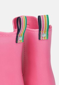 Svetloružové gumáky s textúrovaným povrchom, s viacfarebnými pruhovanými tkaninovými závesmi s kovovými doplnkami pre ľahké obúvanie.