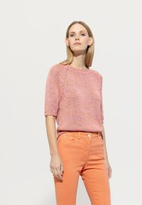 Short-sleeve pink knitted top with a textured design, paired with orange slim-fit jeans featuring a button closure and front pockets.