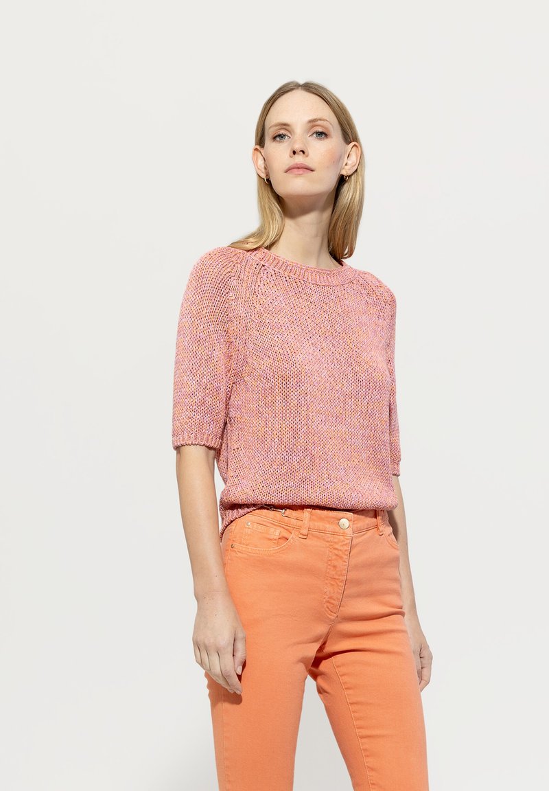Short-sleeve pink knitted top with a textured design, paired with orange slim-fit jeans featuring a button closure and front pockets.