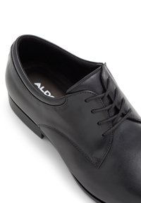 Scarpa da uomo in pelle nera caratterizzata da un'esterno liscio, design con lacci, punta arrotondata e dettagli di cucitura minimi. La suola presenta una leggera lucentezza.