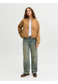 Beige Bomberjacke mit glatter Oberfläche, runder Halslinie und umgeschlagenen Ärmeln, kombiniert mit locker sitzenden hellblauen Jeans und dunklen Schuhen.