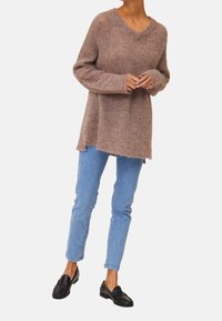 Brun, stickad tröja med V-hals, långa ärmar och en avslappnad passform. Matchad med ljusblå skinny jeans och svarta loafers.
