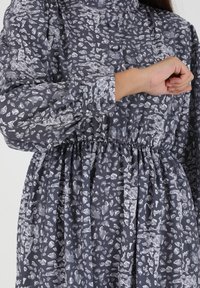 Vestido gris con un patrón de formas abstractas en gris claro y blanco. Presenta una cintura fruncida y mangas largas abullonadas con puños abotonados.