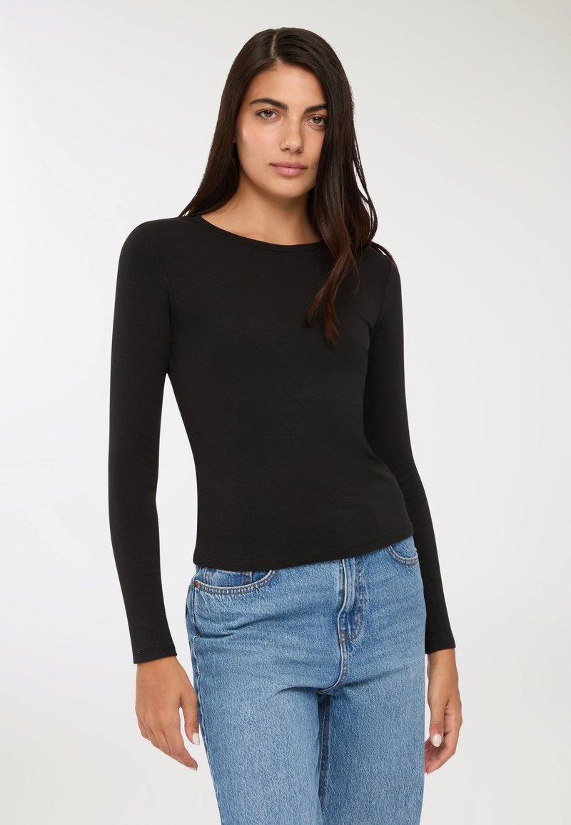 Czarna bluzka z długim rękawem, okrągłym dekoltem, dopasowanym krojem i gładką fakturą, w połączeniu z jasnoniebieskimi dżinsami z wysokim stanem.