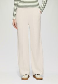Pantalons de jogging larges, de couleur crème, avec poches, fabriqués en tissu doux et texturé. Des coutures descendent à l'avant pour un détail supplémentaire.