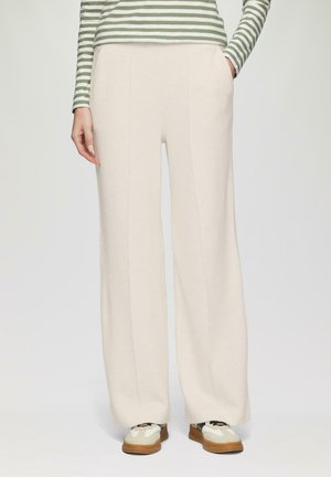 Pantalons de jogging larges, de couleur crème, avec poches, fabriqués en tissu doux et texturé. Des coutures descendent à l'avant pour un détail supplémentaire.