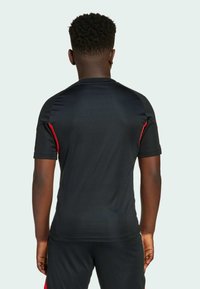 Zwarte sport t-shirt met rode zijkanten, korte mouwen en een getailleerd ontwerp. Soepele, vochtafvoerende stof. Zichtbaar merkl logo op de achterkant.