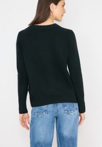 Svart ribbad tröja med långa ärmar och rund halsringning, bärs med ljusblå jeans, som visar en enkel, strukturerad design.