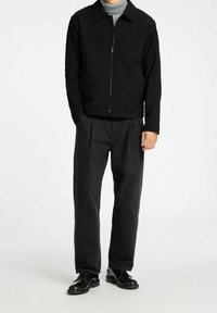 Chaqueta negra con cremallera y cuello con solapa, suéter de cuello alto gris debajo, combinado con pantalones anchos de color gris oscuro y zapatos negros.