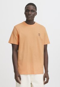 Kratký rukáv tričko z měkké oranžové bavlny s kulatým výstřihem a malou černou grafikou deštníku na hrudi. Volný střih, minimalistický design.