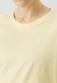 Lys gul bomull t-skjorte med rund hals, korte ermer og en myk, glatt tekstur. Har subtile variasjoner i farge.