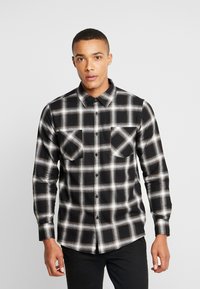 Black and white plaid flannel shirt with a button-down collar, two chest pockets, and long sleeves. Textured fabric with a relaxed fit.