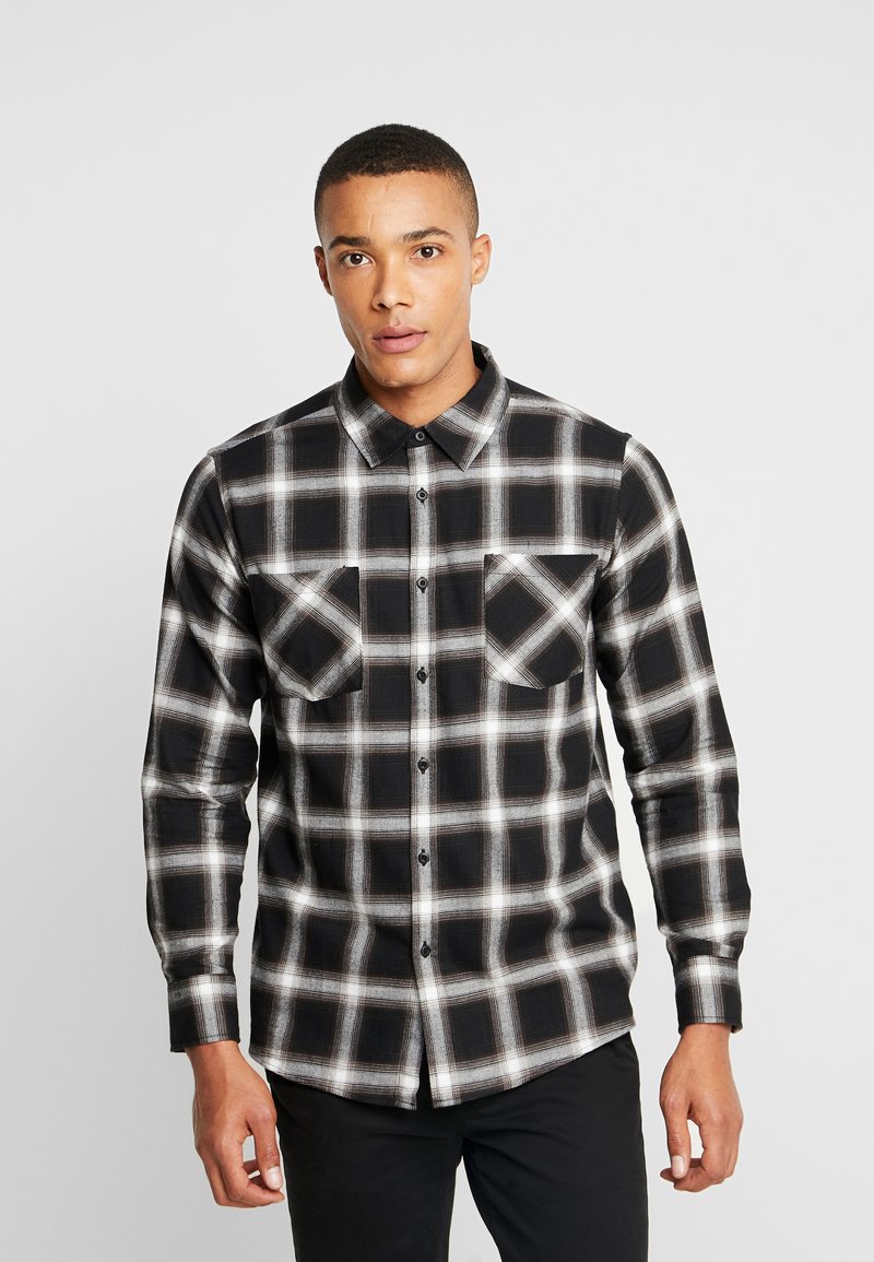 Black and white plaid flannel shirt with a button-down collar, two chest pockets, and long sleeves. Textured fabric with a relaxed fit.