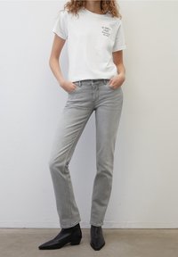 Camiseta blanca con estampado de texto, combinada con unos pantalones vaqueros gris claro y botines negros. Diseño ajustado con detalles sutiles y texturas suaves.