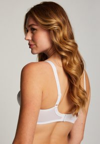 White bra with smooth, structured cups, adjustable straps, and a hook-and-eye closure at the back. Soft fabric with a subtle sheen.