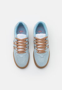 Light blue suede sneakers with brown laces and side stripes. White mesh tongue with red logo, rubber sole, and rounded toe design.