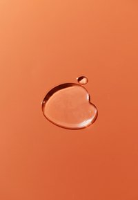 Klar vattendroppe på en orange bakgrund, formad som ett hjärta, med en mindre droppe i närheten, som framhäver den släta texturen och ljusreflektionen.