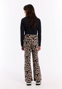 Lerzen met luipaardprint in gedempte beige, bruin en zwarte tinten, met een hoge taille en gedragen met een zwart shirt met lange mouwen en laarzen.