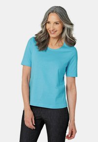 Türkises Baumwoll-T-Shirt mit kurzen Ärmeln und rundem Ausschnitt, kombiniert mit dunkelblauen Jeans. Einfaches Design, ohne Muster oder Akzente.