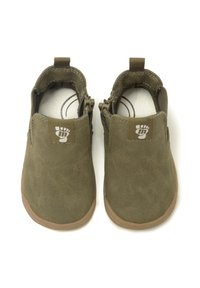 Zapatos de ante de color verde olivo, tipo slip-on, con una suela de goma marrón claro. Presentan un parche con logo en el talón y paneles laterales elásticos para una fácil puesta.