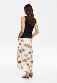 Canotta nera aderente abbinata a una gonna maxi crema con motivi colorati di animali e paisley, completata da sandali neri con fasce.