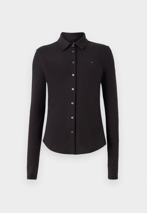 Polo à manches longues noir en tissu doux. Il présente un col, une fermeture à boutons à l'avant et un petit logo brodé sur la poitrine.