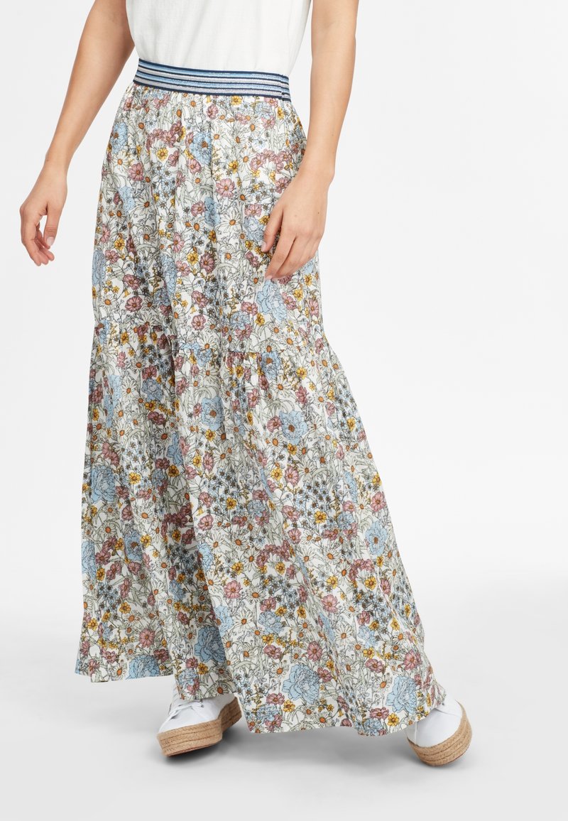 Pantalon large à fleurs bleues, roses et jaunes, associé à des espadrilles compensées blanches et un haut blanc.