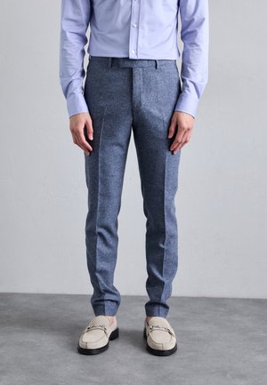 Tailored blue wool trousers with a textured finish and side creases, paired with beige loafers featuring a decorative silver buckle.
