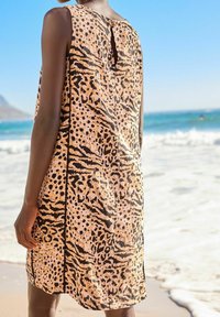 Robe sans manches en tissu beige avec un motif léopard, des accents foncés et un petit détail en forme de trou de serrure au dos.