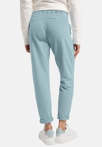 Hellblaue Jogginghosen mit weicher Textur, elastischem Bund mit geprägtem Schriftzug und umgeschlagenen Säumen, kombiniert mit weißen Sneakern.