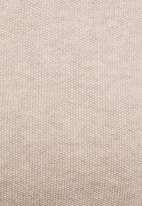 Beżowa dzianina o delikatnej, gładkiej fakturze i subtelnym, jednolitym wzorze. Brak widocznych szwów czy ozdób, co tworzy bezszwowy wygląd.