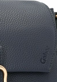 Dunkelblaues, strukturiertes Lederhandtasche mit einem Klappenverschluss. Sie verfügt über goldfarbene Hardware und ein geprägtes Markenlogo, das ein modernes Design bietet.
