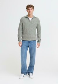 Maglione grigio chiaro con una texture a coste e una chiusura a zip quart. Abbinato a jeans blu e sneakers bianche con strisce nere. Dettaglio del logo semplice.