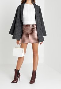 Szara marynarka w kratę, biały prążkowany top, różowa mini spódnica w kratę, biała torebka oraz bordowe botki za kostkę z zamkami i obcasami.