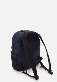 Zaino blu navy con un'esterno in nylon liscio, spallacci neri regolabili, chiusura superiore con zip e una tasca laterale in rete per ulteriore spazio di stoccaggio.