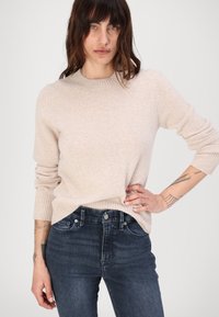 Beżowy sweter prążkowany z okrągłym dekoltem i długimi rękawami, zestawiony z ciemnymi dżinsami. Materiał wydaje się miękki i luźny, co zapewnia swobodny fason.