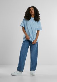 Lyseblå stripete t-skjorte med korte ermer, kombinert med oversized blå jeans og hvite joggesko. Myk stoff med en avslappet passform.