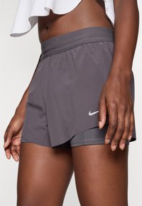 Grå treningsshorts med elastisk midje, lagdelt design og indre fôr. Har en liten hvit Nike-logo på siden.