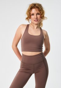Barna sportos crop top széles vállpántokkal, magas derekú leggingsszel párosítva. Simulékony, rugalmas anyag kontrasztos varrási részletekkel.